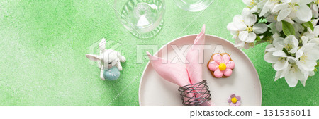 A beautifully arranged table setting for Easter features a pink napkin wrapped around an egg, surrounded by floral decorations and colorful candies, banner A beautifully arranged table setting for Easter features a pink napkin wrapped around an egg, surrounded by floral decorations and colorful candies, banner 131536011