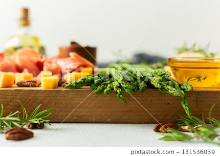 A vibrant charcuterie board is set for a gathering, showcasing fresh asparagus, assorted cheeses, cured meats, and nuts. This setup invites guests to enjoy tasty bites together 131536039