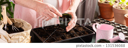 In a cozy home setting, a man carefully plants tomato seeds into small pots, surrounded by gardening tools and seed packets, eagerly preparing for spring gardening, banner In a cozy home setting, a man carefully plants tomato seeds into small pots, surrounded by gardening tools and seed packets, eagerly preparing for spring gardening, banner 131536088