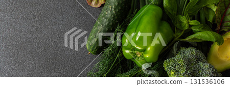 A variety of fresh green vegetables is neatly arranged on a dark surface, showcasing cucumbers, bell pepper, avocado, broccoli, and various leafy greens, healthy eating for a nutritious salad, banner A variety of fresh green vegetables is neatly arranged on a dark surface, showcasing cucumbers, bell pepper, avocado, broccoli, and various leafy greens, healthy eating for a nutritious salad, banner 131536106