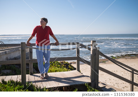 Middle-aged woman sitting on a wall looking at the ocean in Portugal, enjoying a sunny summer day 131536380