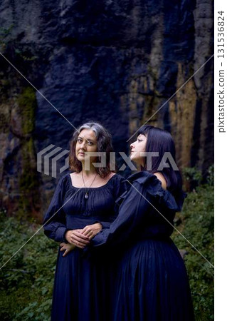 two women in the black long dresses sitting on black rocks on Halloween, performing a witch ritual, modern witch two women in the black long dresses sitting on black rocks on Halloween, performing a witch ritual, modern witch 131536824