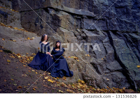 two women in the black long dresses sitting on black rocks on Halloween, performing a witch ritual, modern witch two women in the black long dresses sitting on black rocks on Halloween, performing a witch ritual, modern witch 131536826