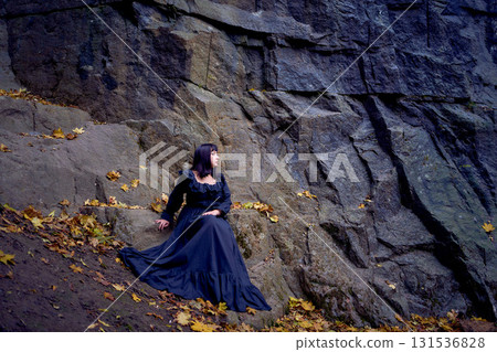 a woman in a black long dress sitting on black rocks on Halloween, modern witch a woman in a black long dress sitting on black rocks on Halloween, modern witch 131536828