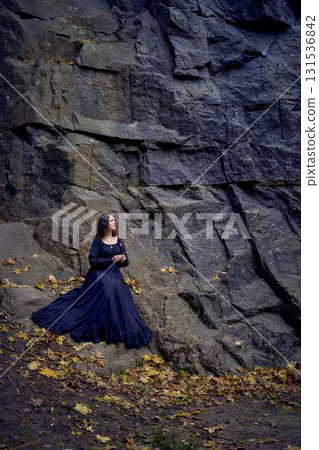 woman in a black long dress sits on black rocks on Halloween holding a burning candle, performs a witch ritual, modern witch woman in a black long dress sits on black rocks on Halloween holding a burning candle, performs a witch ritual, modern witch 131536842