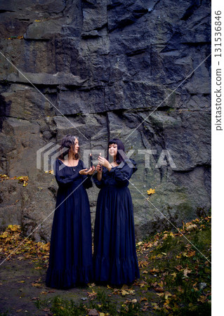 two women in the black long dresses near black rocks on Halloween holding a burning candle, performing a witch ritual, modern witch 131536846