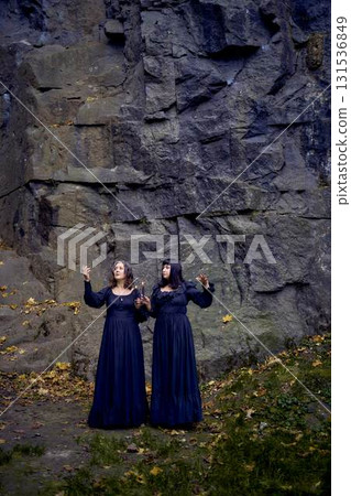 two women in the black long dresses near black rocks on Halloween holding a burning candle, performing a witch ritual, modern witch 131536849