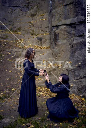 two women in the black long dresses near black rocks on Halloween holding a burning candle, performing a witch ritual, modern witch 131536851