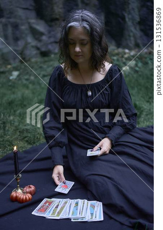 two women in black long dresses sitting on the black rocks on Halloween, reading tarot cards, performing a witch ritual, modern witch 131536869
