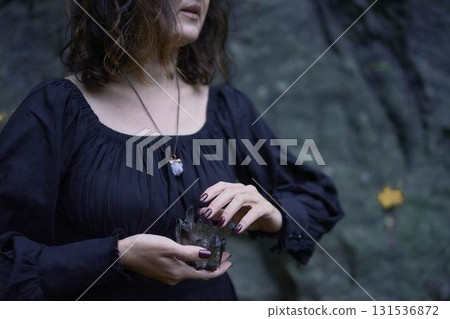 a woman in a black long dress near black rocks on Halloween holding a purple black crystal, performing a witch ritual, modern witch a woman in a black long dress near black rocks on Halloween holding a purple black crystal, performing a witch ritual, modern witch 131536872