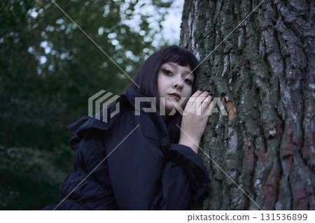 Two women in the long black dresses perform a historical reenactment of the Edwardian era on a hill near a majestic oak tree for Halloween. 131536899