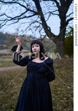 a women in the long black dresses perform a historical reenactment of the Edwardian era on a hill near a majestic oak tree for Halloween. 131536913