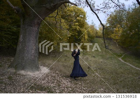 a women in the long black dresses perform a historical reenactment of the Edwardian era on a hill near a majestic oak tree for Halloween. 131536918