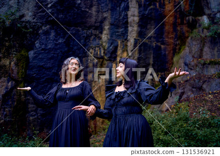 two women in the black long dresses sitting on black rocks on Halloween, performing a witch ritual, modern witch two women in the black long dresses sitting on black rocks on Halloween, performing a witch ritual, modern witch 131536921