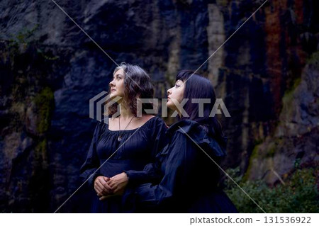 two women in the black long dresses sitting on black rocks on Halloween, performing a witch ritual, modern witch 131536922