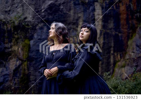 two women in the black long dresses sitting on black rocks on Halloween, performing a witch ritual, modern witch two women in the black long dresses sitting on black rocks on Halloween, performing a witch ritual, modern witch 131536923