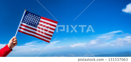A child's hand is holding a small American flag against a blue sky. A child's hand is holding a small American flag against a blue sky. 131537063