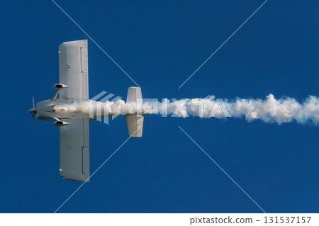 Stunt aerobatic plane performing stunts in blue sky with smoke trail. Concept of speed, difficulty, precision, risk, challenge 131537157