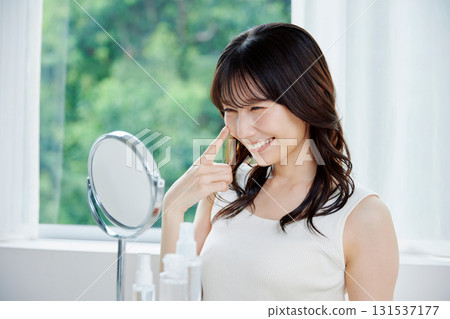 Smiling woman checking her skin condition in the mirror 131537177