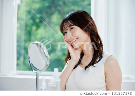 微笑的女人對著鏡子檢查自己的皮膚狀況 微笑的女人對著鏡子檢查自己的皮膚狀況 131537178