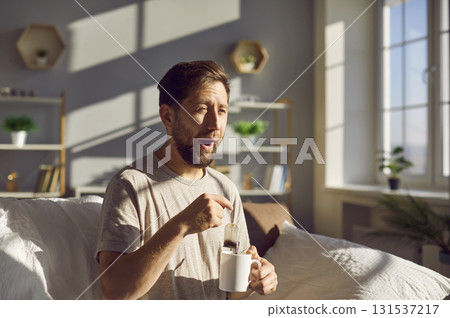 Sleepy man just waking up brewing tea in a cup and yawning in the morning. 131537217