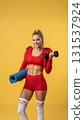 fit woman is showcasing her strength while holding a dumbbell in one hand and a yoga mat in the other. 131537924