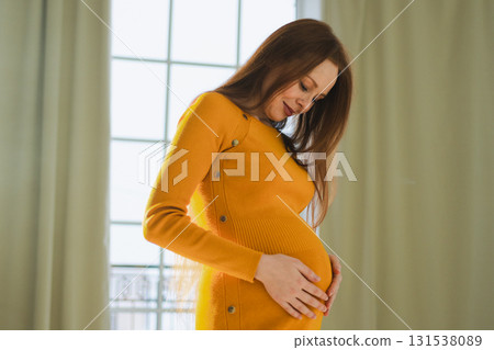 Pregnancy motherhood people expectation future. Pregnant woman with big belly standing near window at home. Girl hugging her tummy enjoying pregnancy. Maternity tenderness parenthood new life concept Pregnancy motherhood people expectation future. Pregnant woman with big belly standing near window at home. Girl hugging her tummy enjoying pregnancy. Maternity tenderness parenthood new life concept 131538089