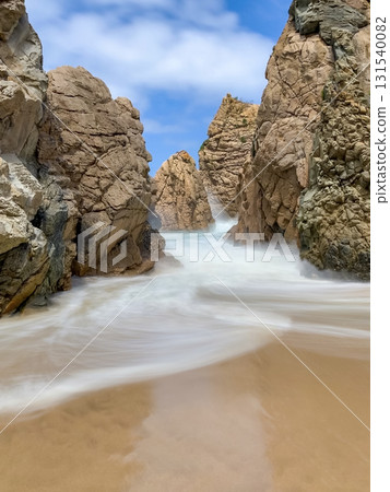 Ursa beach near Cabo da Roca features rugged cliffs, golden sand, and crashing waves under a clear blue sky. Long exposure photography Ursa beach near Cabo da Roca features rugged cliffs, golden sand, and crashing waves under a clear blue sky. Long exposure photography 131540082