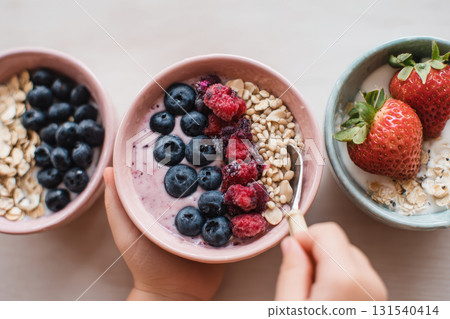 Smoothie bowl with yogurt blueberry raspberry oat grain strawberry healthy breakfast fresh fruit closeup hand holding spoon delicious and nutritious meal 131540414
