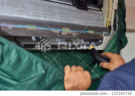 male hand of worker from the cleaning service cleans the air conditioner by spraying water, close-up 131541736