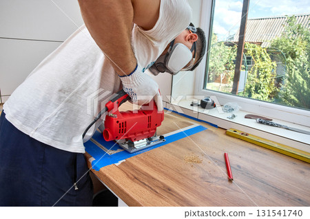repairman using electric jigsaw and cutting hole for the sink in the kitchen countertops 131541740