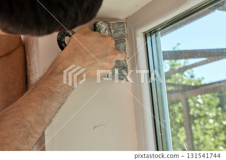 Caucasian plasterer man with a spatula applying finishing putty on a window opening 131541744