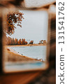 Autumn lake landscape framed. An autumn park and river is reflected. The lake and autumnal trees show the warm colors of the season under a cloudy sky 131541762