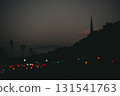 Cityscape silhouette at dusk with blurred lights. A dark abstract and moody cityscape silhouette is set against a dusky sky, with blurred city lights adding a touch of color to the scene Night traffic 131541763