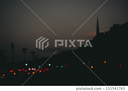 Cityscape silhouette at dusk with blurred lights. A dark abstract and moody cityscape silhouette is set against a dusky sky, with blurred city lights adding a touch of color to the scene Night traffic 131541763