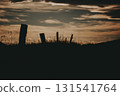 Silhouette of fence posts against a dramatic sunset sky. A moody serene landscape captures the silhouette of weathered fence posts set against a vibrant, cloud-filled sunset, creating a tranquil scene 131541764