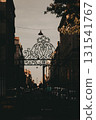 Ornate gate leading to a city street. An elegant wrought iron gate frames a view down a city street, with buildings lining the road and soft light. Vertical moody shot of an old French town, Bordeauxe 131541767