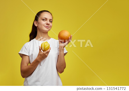 happy woman holding fresh lemon and grapefruit on yellow studio background 131541772