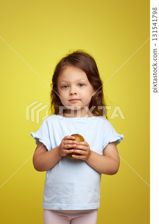 cute Caucasian little child girl holding kiwi fruit on yellow background 131541798