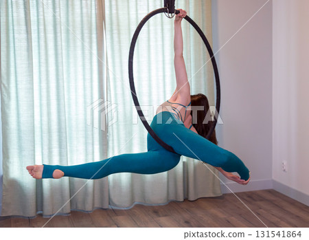 A young woman is engaged in antigravity yoga with a hoop. 131541864