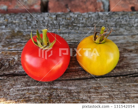 Two ripe tomatoes, one red and one yellow, on a wooden table in the garden Two ripe tomatoes, one red and one yellow, on a wooden table in the garden 131542054