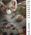 Female hands making Christmas decoration with candle, spruce needles, jute twine on a wooden background, vertical image. 131542378