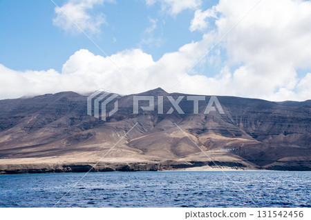 一片寬闊波濤洶湧的海洋,遠處是一座棕色的光禿禿的山峰。這是加那利群島富埃特文圖拉島的海上。 一片寬闊波濤洶湧的海洋,遠處是一座棕色的光禿禿的山峰。這是加那利群島富埃特文圖拉島的海上。 131542456