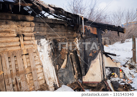 A wooden building shows severe fire damage, with charred walls and a collapsing roof, surrounded by snow. Icicles hang from the remnants, a cold winter day A wooden building shows severe fire damage, with charred walls and a collapsing roof, surrounded by snow. Icicles hang from the remnants, a cold winter day 131543340