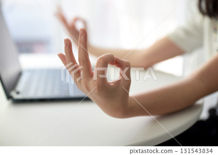 Close up image of woman's hands who was sitting and meditating at his desk in a white office To meditate to calm the mind and relax before starting work. The room is bright with natural light. Close up image of woman's hands who was sitting and meditating at his desk in a white office To meditate to calm the mind and relax before starting work. The room is bright with natural light. 131543834