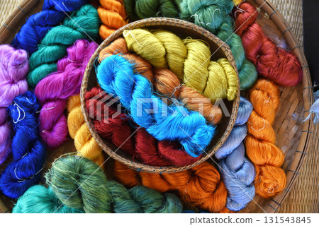 Tie of colorful and shiny beautiful silk yarn dyed placed in a pile of round bamboo baskets. Prepared for use as a raw material for weaving silk. 131543845