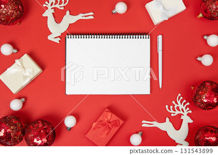 Christmas composition of gift boxes and toys on Christmas tree, with an open blank notebook and pen on red background for writing goals and plans for the New Year. Flat lay, copy space 131543899