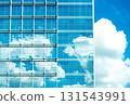 Glass office facade reflects blue sky and cumulus clouds, merging city and nature. 131543991