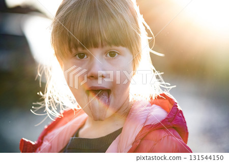 Portrait of a pretty child girl showing her tongue outdoors. 131544150