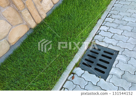 Plastic drain gutter, green grass lawn and stone pavement sidewalk. 131544152